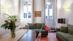 Un salon avec un canapé vert, une table à manger en bois ornée d’un vase de fleurs et un téléviseur posé sur une commode.