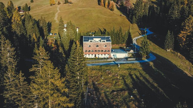 Una vista aerea di un edificio a più piani circondato da una fitta foresta, con una strada tortuosa che vi conduce.