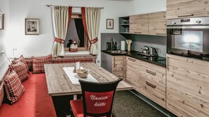 Una cucina compatta con mobili in legno, forno a incasso e zona pranzo con divano rosso e cuscini abbinati.