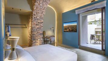 Une chambre d’hôtel avec un grand lit, un bureau, une chaise et une vue sur la ville, visible à travers une porte vitrée.