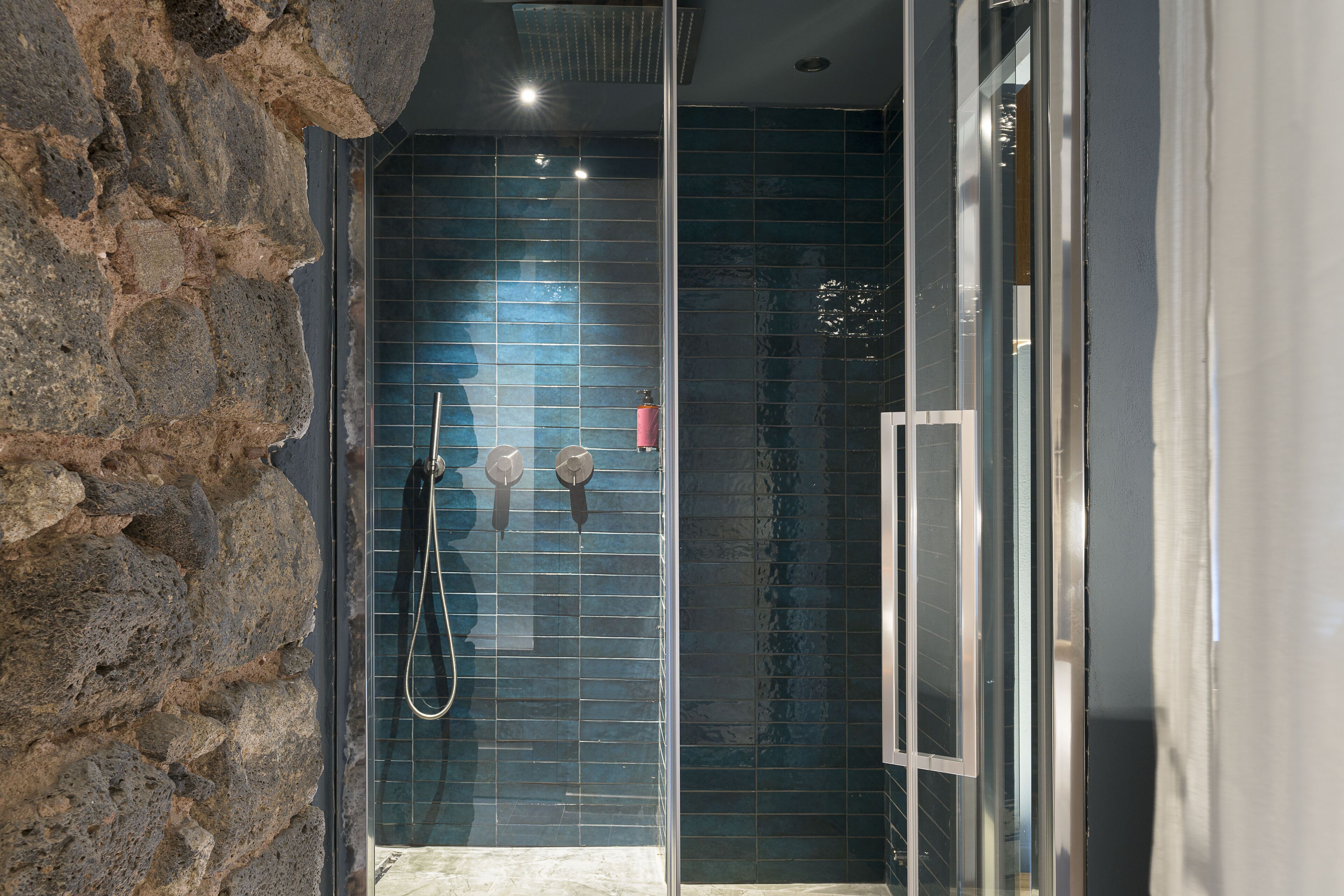 A glass-enclosed shower with a stone wall on one side.