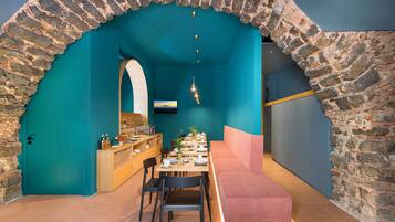 Un restaurante con un arco de piedra, paredes azul verdoso y una larga mesa de madera con sillas.