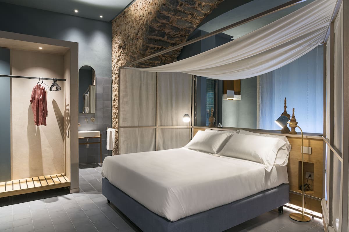 A modern bedroom with a large bed, a wooden nightstand, a mirror, and a stone accent wall.