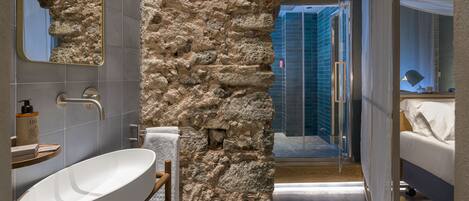 Une salle de bain moderne avec une baignoire sur pieds, un mur d’accent en pierre et une douche à parois de verre.