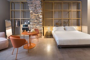 Habitación de hotel moderna con una cama grande, una pequeña mesa redonda con dos sillas, una pared de acento de piedra y una estantería de madera.