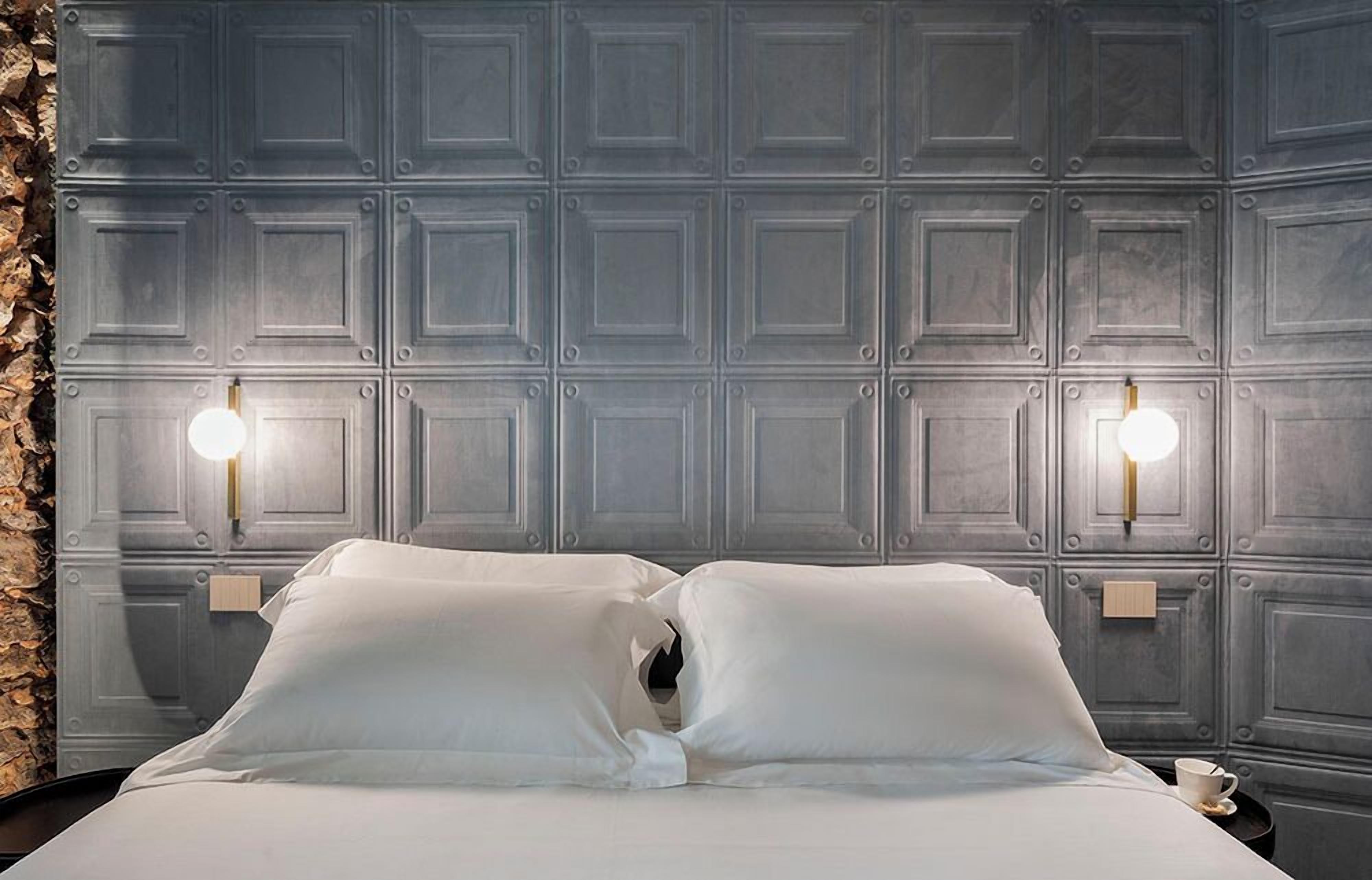 Ein Hotelzimmer mit einem grossen Bett, zwei Wandleuchten und einer Wand aus Stein.