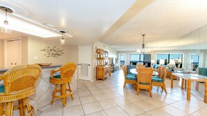 Amplia sala de estar con muebles de mimbre, una mesa de comedor y una cocina al fondo.