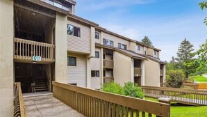 A multi-story residential building with balconies, a covered entrance, and a wooden fence. - Pinnacle C03 Condo | Pool, Hot Tub | Golf Nearby (Killington)
