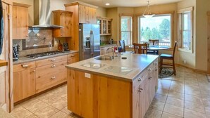 A spacious kitchen with wooden cabinets, a central island, and a dining area with a table and chairs. - Cascade Cabin Overlooking Lake & Golf Course (Cascade)