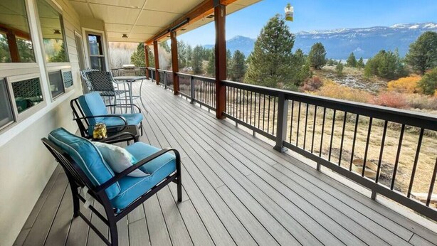 A covered balcony with two blue cushioned chairs and a table, overlooking a mountainous landscape. - Cascade Cabin Overlooking Lake & Golf Course (Cascade)