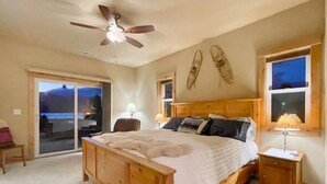 A bedroom with a wooden bed, a ceiling fan, a nightstand, and a view through a sliding door. - Cascade Cabin Overlooking Lake & Golf Course (Cascade)