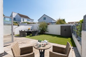 Un espace patio aménagé avec des meubles en osier, une petite table ronde et une pelouse.