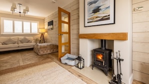 A cozy living room with a fireplace, a sofa, a rug, and a door leading to another room. - Out of the Blue: Spacious pet-friendly holiday home in Rhosneigr (Rhosneigr)