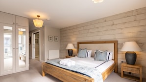 A bedroom with a wooden bed, two bedside lamps, a nightstand, a bench, a wardrobe, and a view of a balcony. - Out of the Blue: Spacious pet-friendly holiday home in Rhosneigr (Rhosneigr)