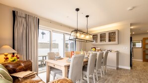 A modern dining area with a wooden table, cushioned chairs, and a hanging light fixture. - Out of the Blue: Spacious pet-friendly holiday home in Rhosneigr (Rhosneigr)