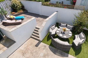 A rooftop patio with a sun lounger, a round dining table with chairs, and a small garden area. - Out of the Blue: Spacious pet-friendly holiday home in Rhosneigr (Rhosneigr)