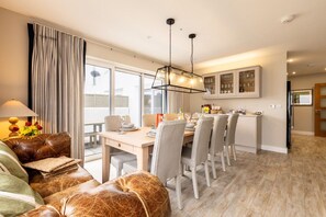A modern dining area with a wooden table, grey upholstered chairs, and a hanging light fixture. - Out of the Blue: Spacious pet-friendly holiday home in Rhosneigr (Rhosneigr)