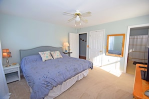 A bedroom with a bed, nightstand, lamp, ceiling fan, and a door leading to a bathroom.