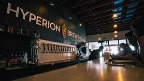 Un'area bar con un cartello che indica 'Hyperion Brewing', un bancone con rubinetti e una zona con tavoli.
