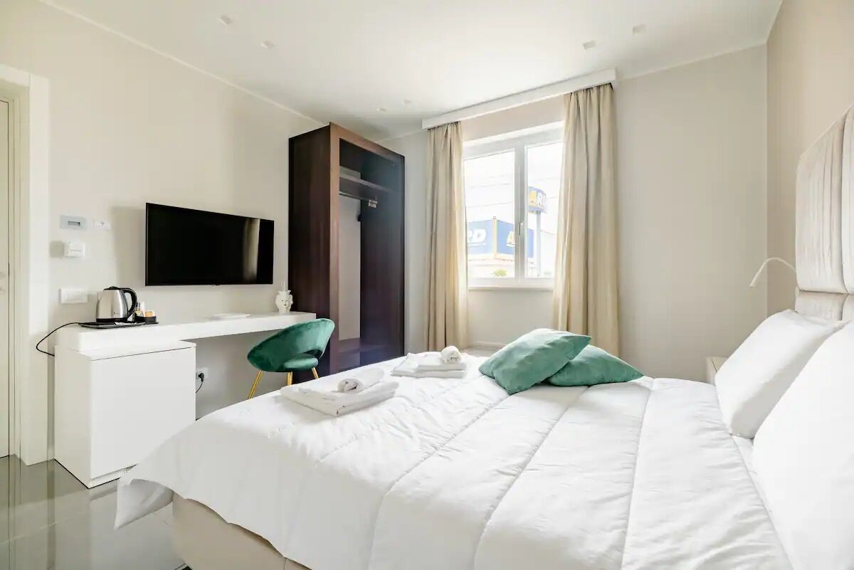 Quarto de hotel com uma cama, uma escrivaninha com televisão de tela plana, um guarda-roupa e uma janela com cortinas.