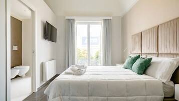 Ein modernes Schlafzimmer mit einem großen Bett, einem Flachbildfernseher, einem Fenster mit Vorhängen und Blick ins Freie.