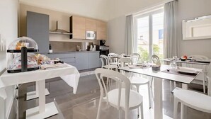 A modern kitchen with a microwave, cabinets, and a dining area with white chairs and a glass table. - SHoruq (Marsala)