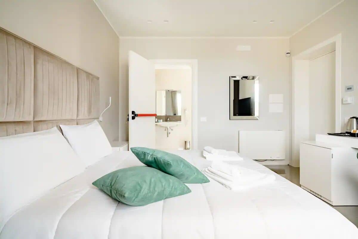 A modern hotel room with a large bed, a bedside table, a mirror, and a view into the bathroom.