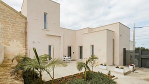 A modern building with a courtyard, featuring a brick wall, a white door, and a small table with chairs. - SHoruq (Marsala)