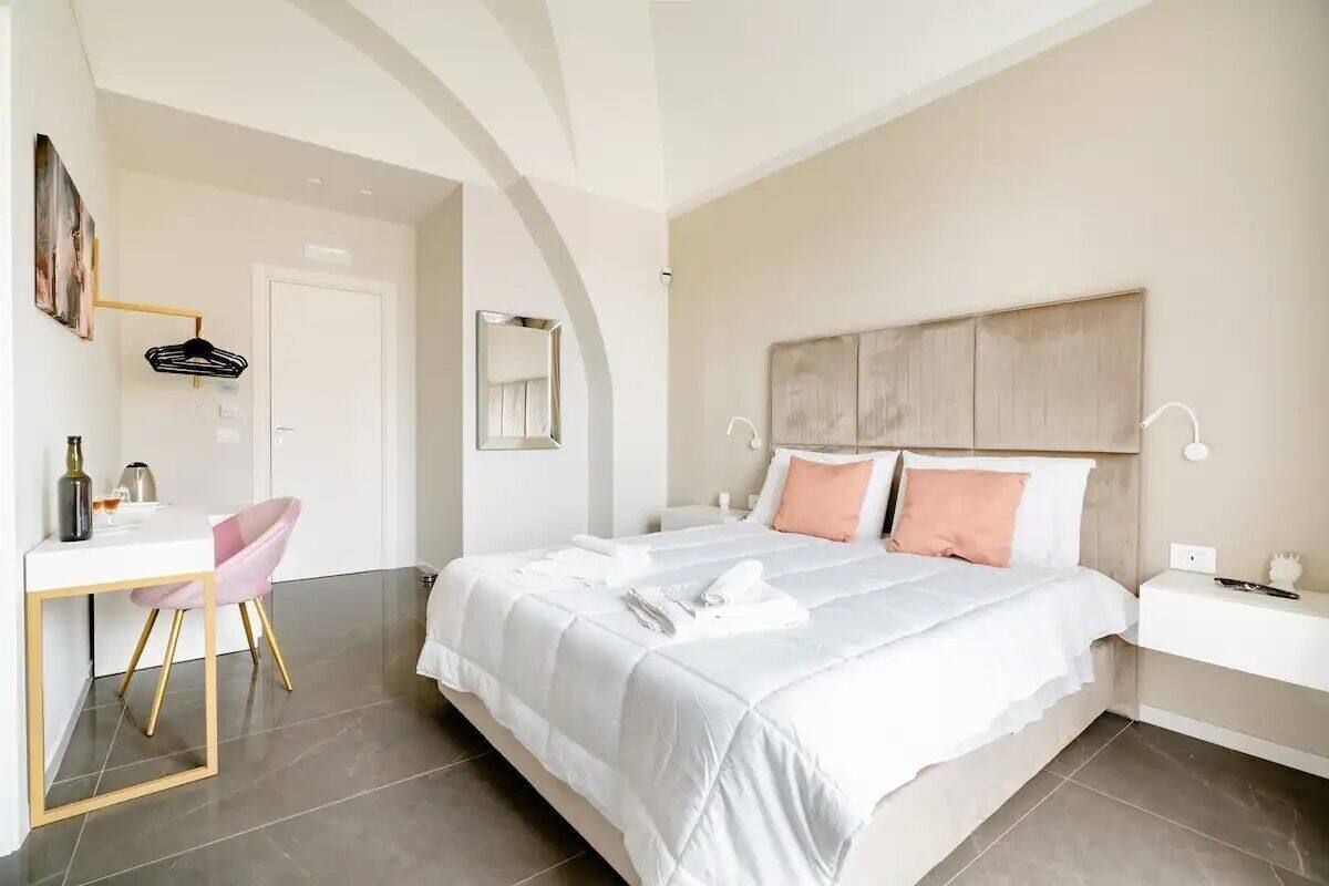 A bedroom with a bed, bedside table, chair, desk, and a door.