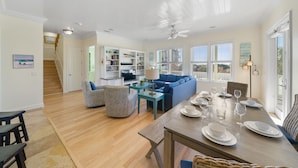 A spacious living area with a blue sofa, wooden dining table set for four, and a bookshelf filled with books. - "Surfer Dog" | Beachfront Pool | Includes Beach Chairs & Bikes (Inlet Beach)