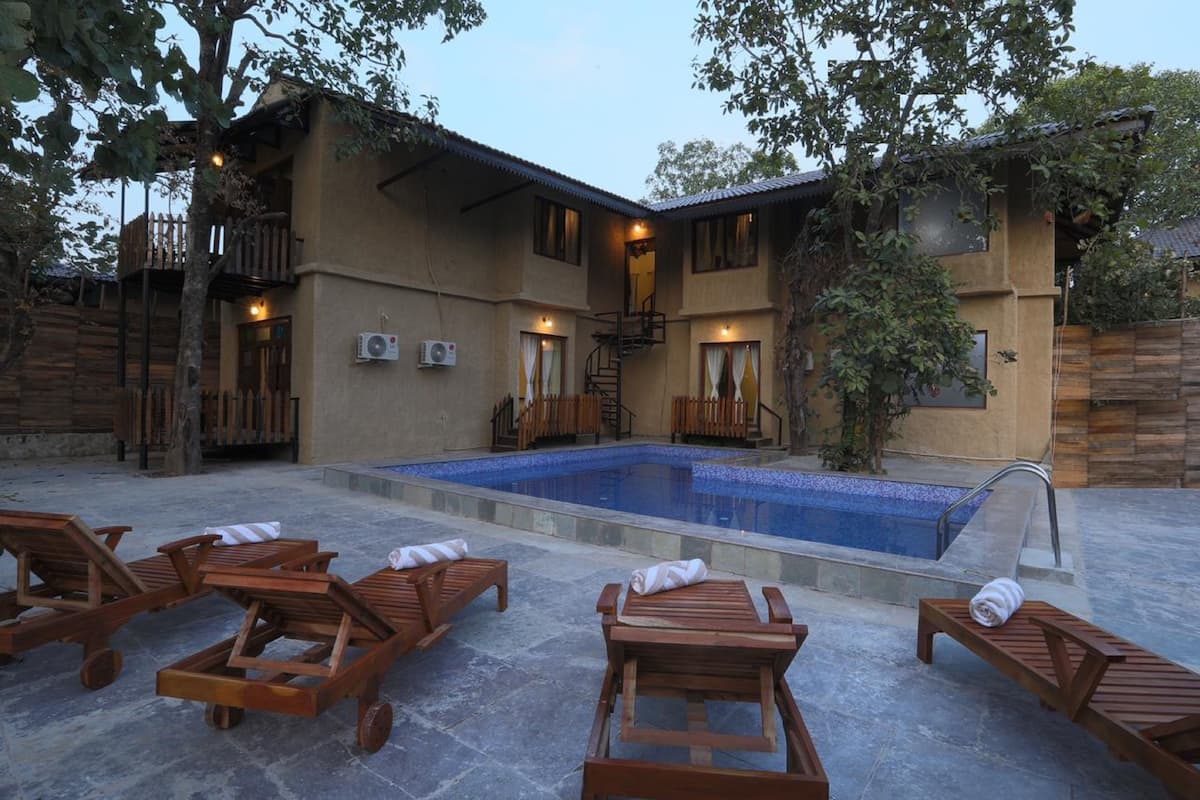 A poolside area with wooden loungers, a small pool, and a building with a staircase and windows.