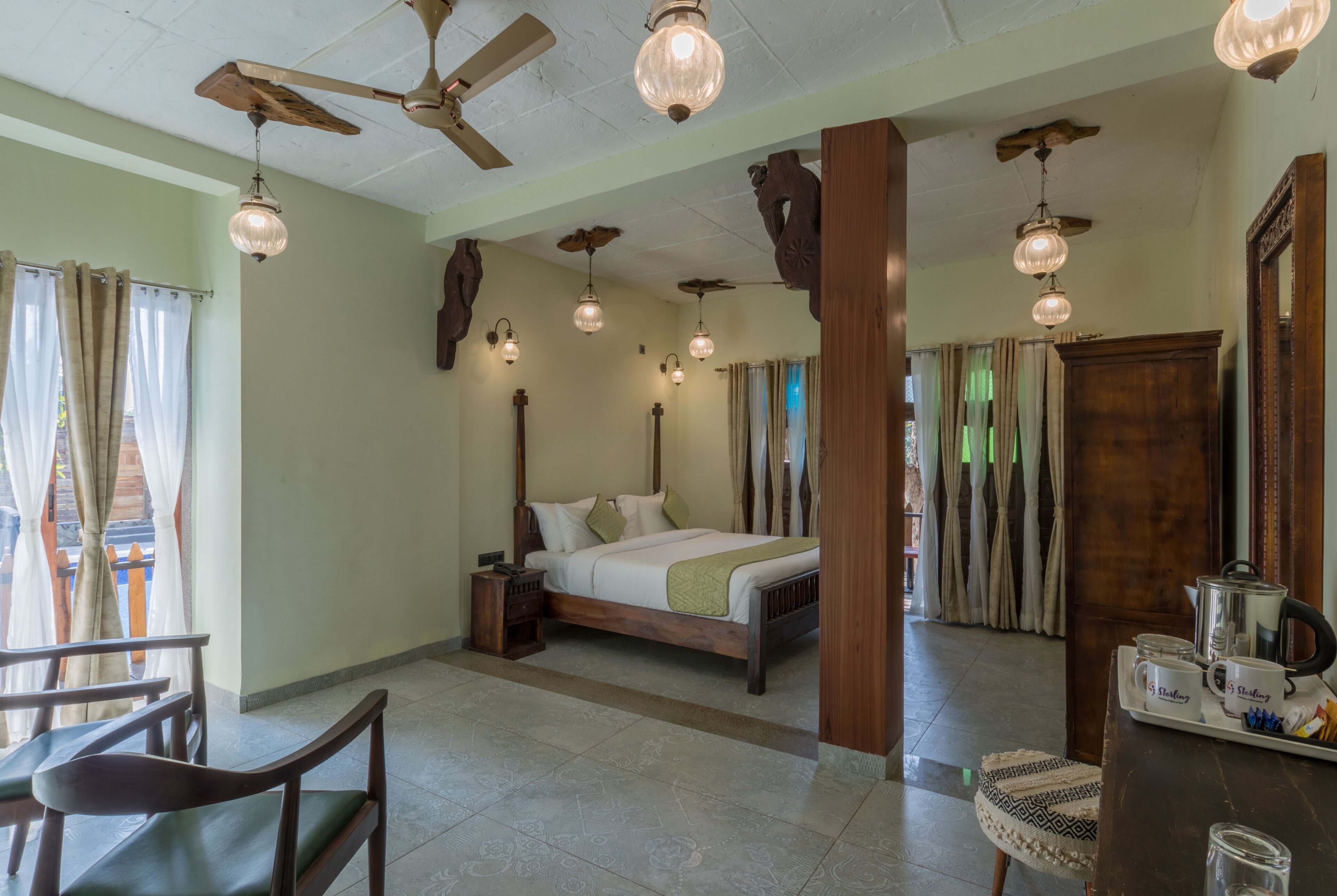 A bedroom with a wooden bed, a nightstand, a chair, a table with a tray of items, and a ceiling fan.
