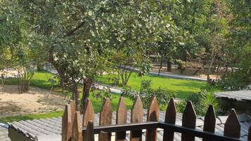Vista desde un balcón con valla de madera, zona verde y árboles al fondo.