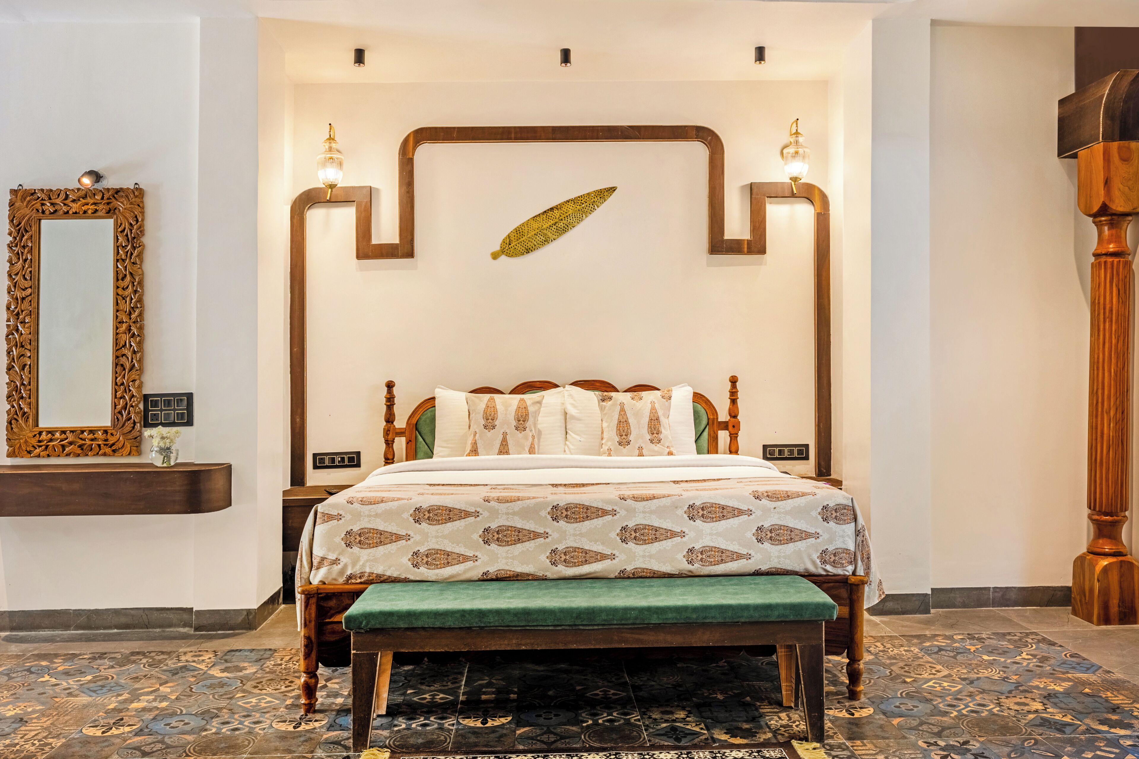 A bedroom with a wooden bed, a green bench, patterned carpet, a decorative leaf, and a mirror.