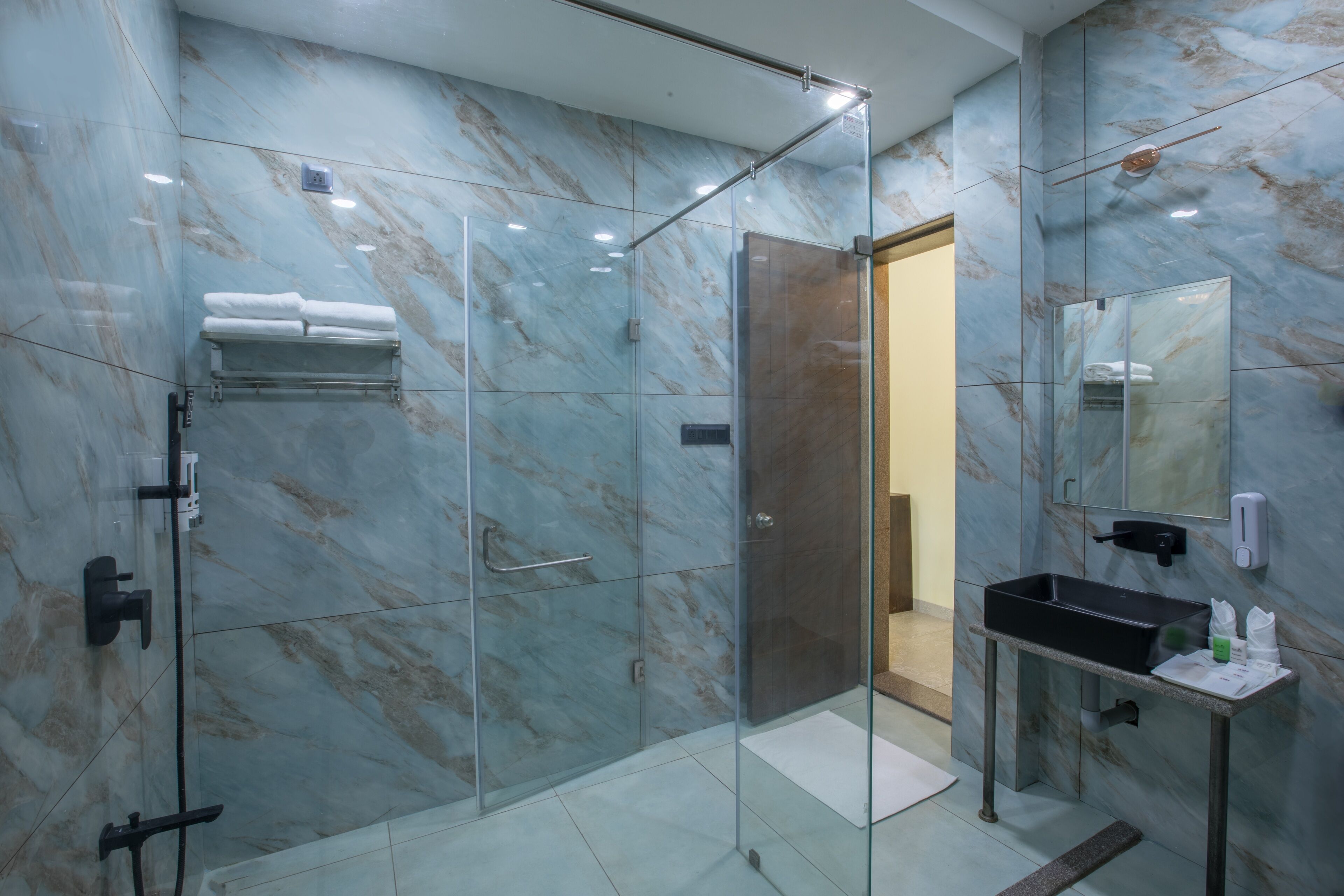 A modern bathroom with a glass-enclosed shower, marble walls, and a black sink with toiletries.