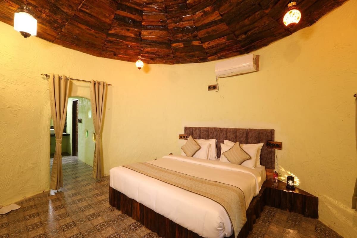A bedroom with a wooden ceiling, a bed with white bedding, a nightstand, and an air conditioning unit on the wall.