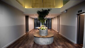 Eine moderne Hotelhalle mit einem zentralen Blumentopf, Holzboden und einem Schild, das den Weg zu den Toiletten zeigt.