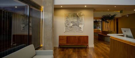 Una zona de recepción moderna con un banco de madera, un mostrador de recepción y una gran obra de arte abstracta en la pared.