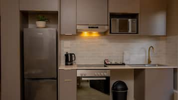 A compact kitchen with a stainless steel refrigerator, a microwave, an oven, and a sink with a gold faucet.