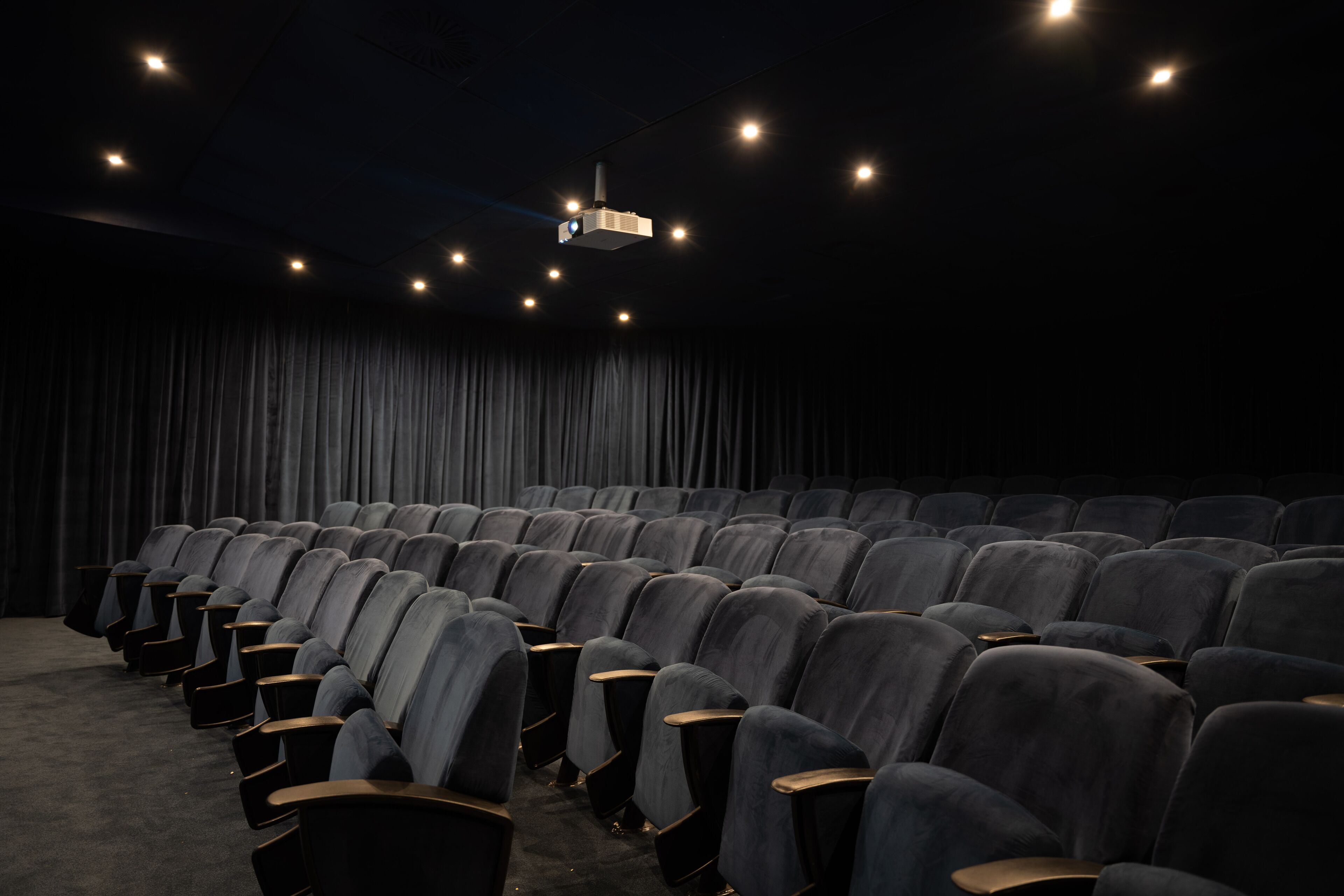 A theater with rows of seats, a dark curtain backdrop, and a ceiling projector.