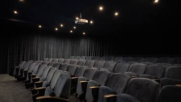 A theater with rows of seats, a dark curtain backdrop, and a ceiling projector.