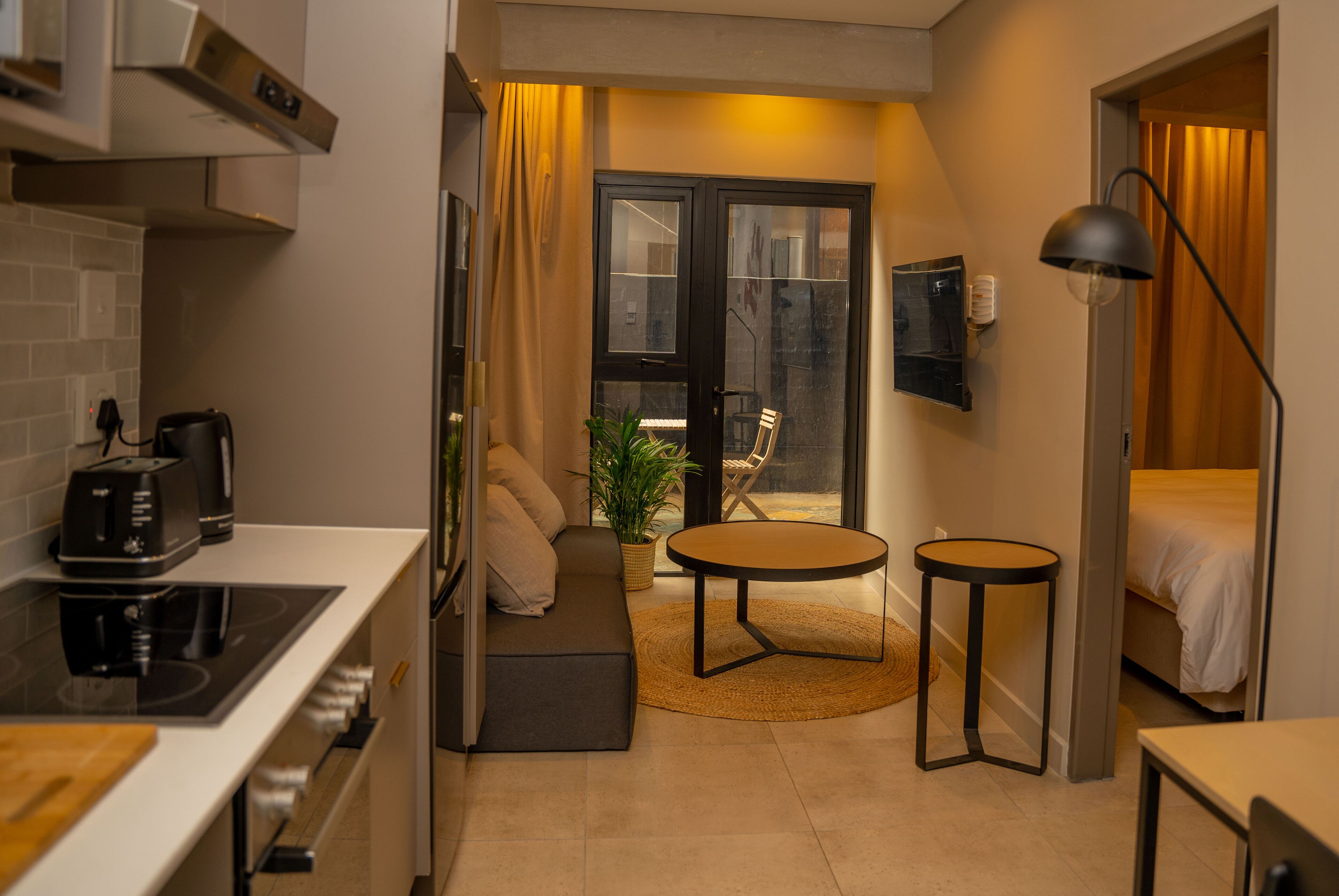 A compact hotel room with a kitchenette, a sofa, a small round table, a bed, and a TV.