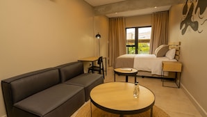 Ein modernes Hotelzimmer mit einer Couch, einem runden Tisch, einem Bett und Blick ins Freie.
