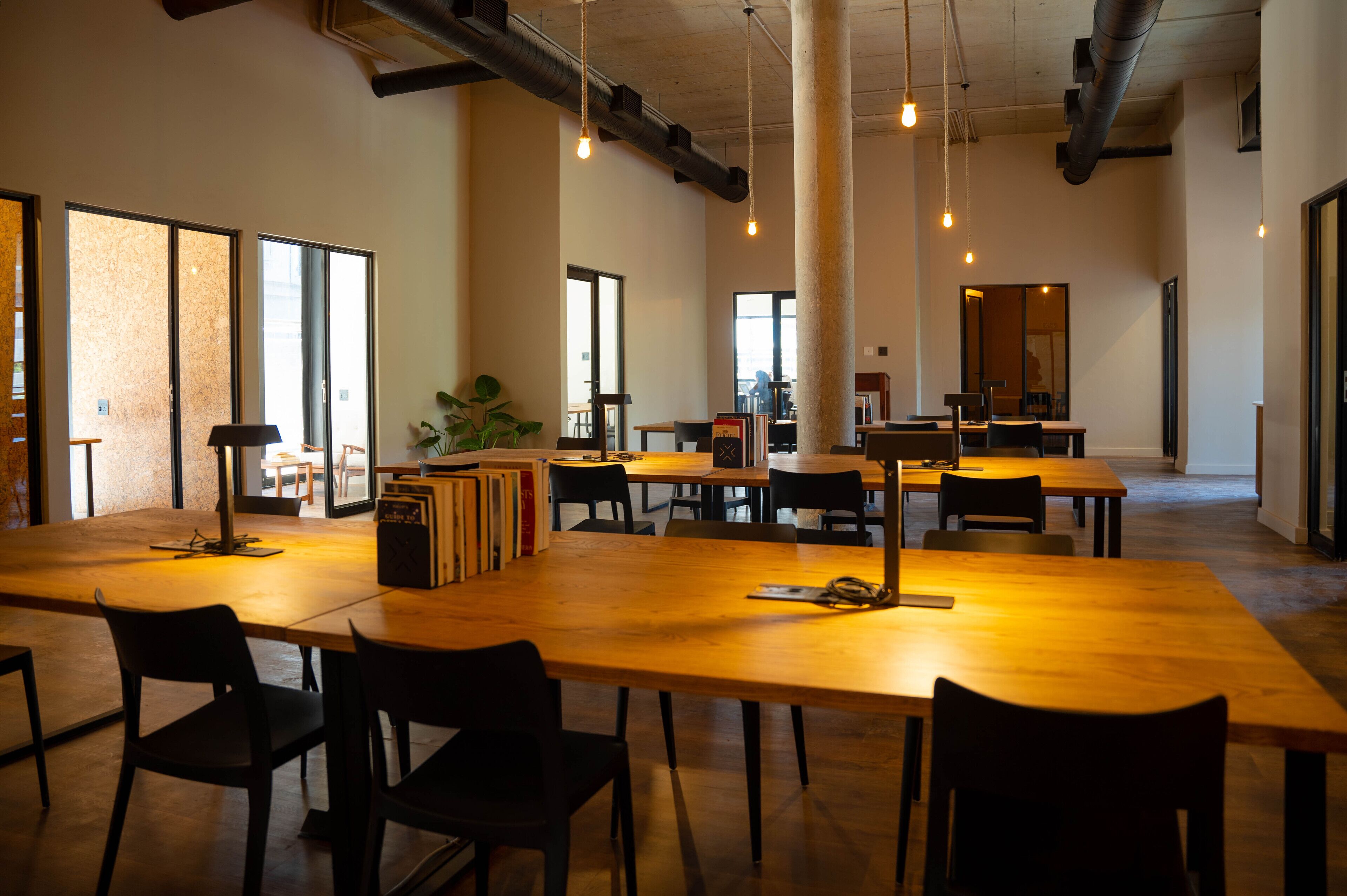 A spacious, well-lit meeting room with large tables and chairs, high ceilings, and visible ductwork.