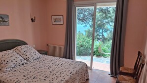 Une chambre à coucher comprenant un lit, une chaise, un radiateur et une vue sur un jardin, accessible par une porte coulissante.