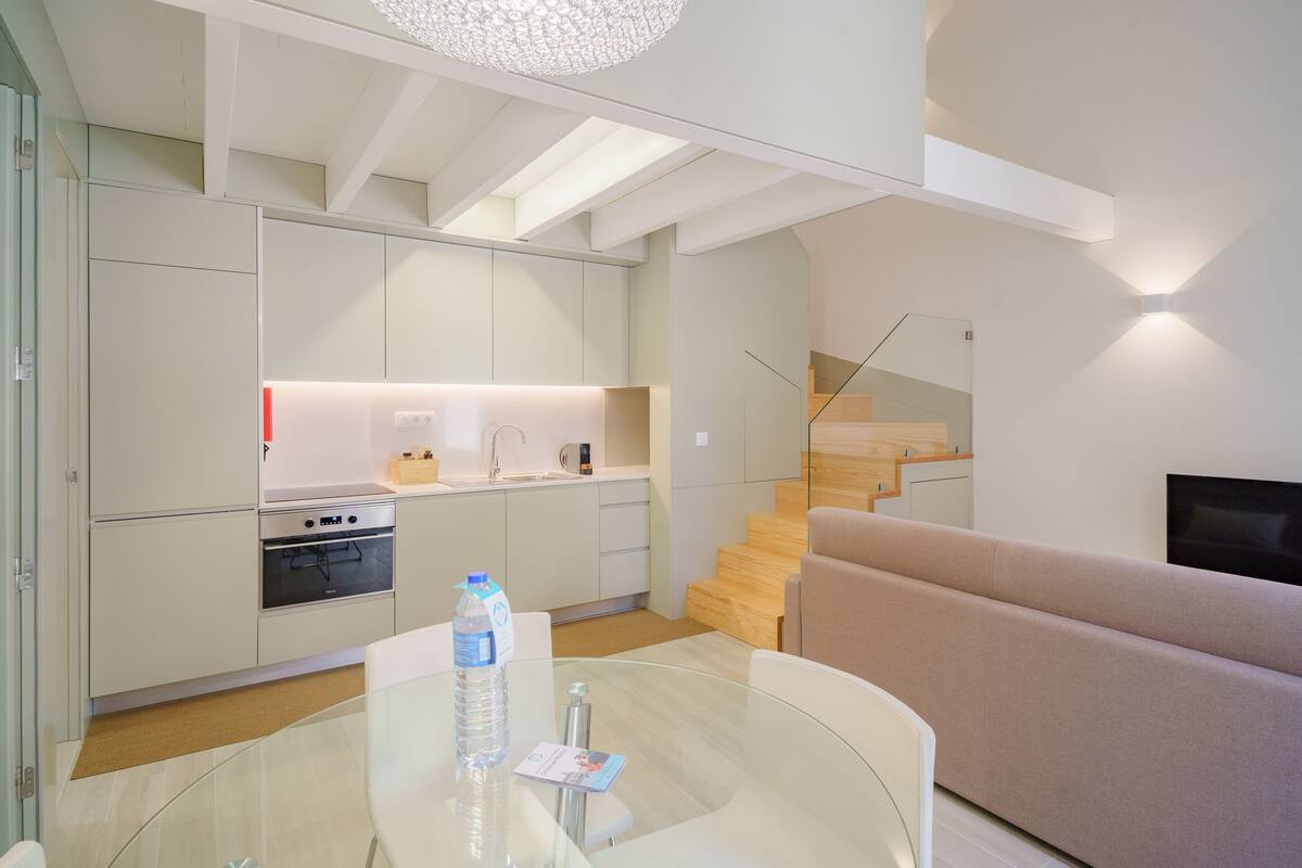 Una cocina moderna con electrodomésticos integrados, una mesa de comedor de vidrio y una escalera que sube a un nivel superior.