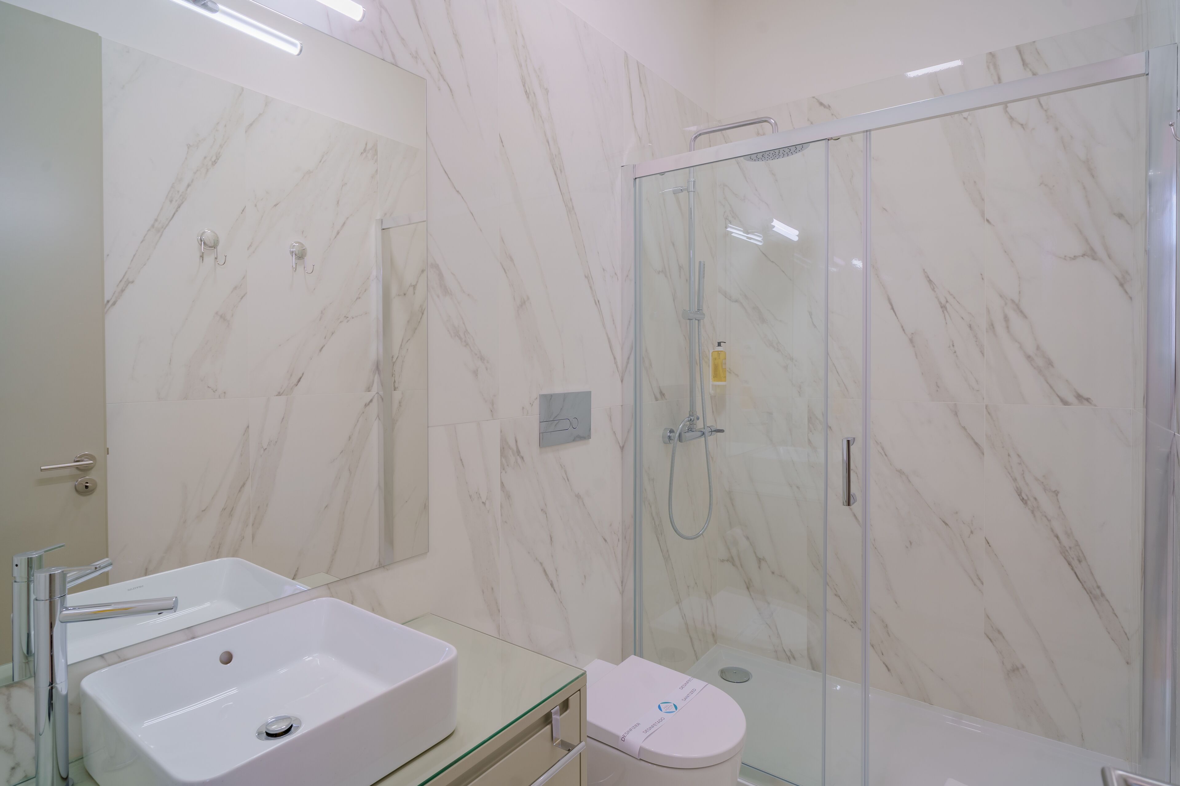 Un baño moderno con ducha de vidrio, un lavamanos blanco y un inodoro.