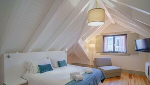 Ett sovrum med en säng, en stol, en tv och ett fönster med gardiner.