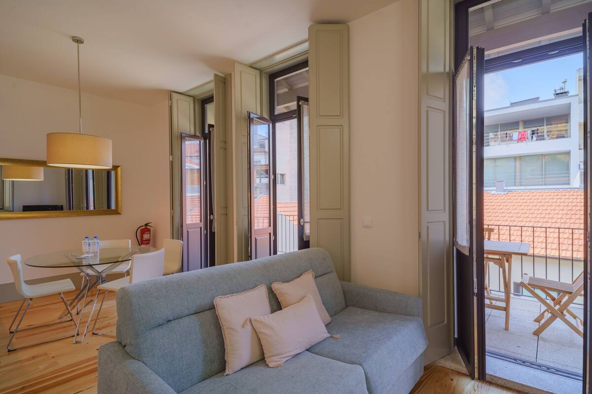 Una sala moderna con un sofá gris, una mesa de vidrio y un comedor con sillas.