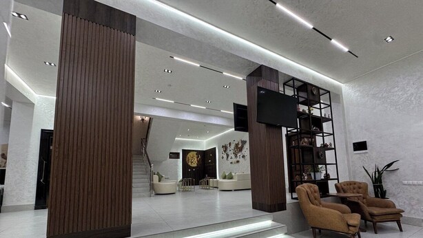 Eine moderne Lobby mit einer Treppe zu einer zweiten Etage, ausgestattet mit einer Sitzecke mit Sofas und Sesseln, einer Holzsäule und einem schwarzen Regalschrank.